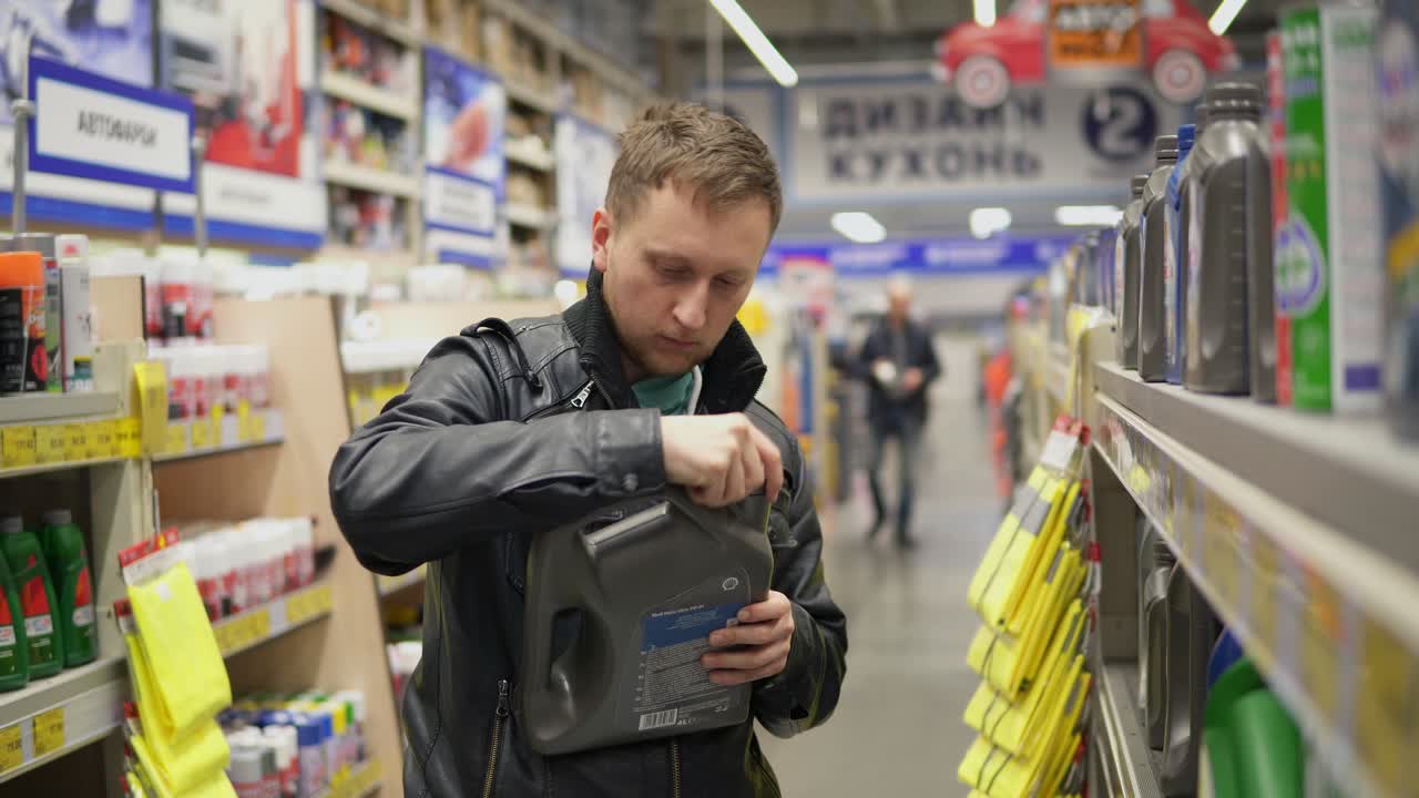 젊은이 는 수리 서비스 스테이션 이나 슈퍼마켓 에서 자동차 를 위한 모터 오일 을 선택 하고 있다. 선반 에 있는 여러 가지 통 들