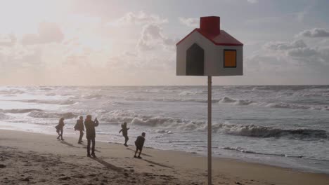 Silueta-De-Familia-Feliz-Jugando-Con-El-Viento-En-La-Playa-Con-Un-Poste-De-Orientación-En-Primer-Plano---De-Haan,-Bélgica