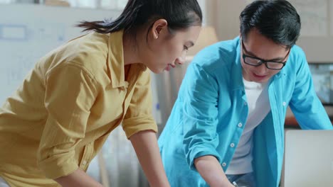 asian woman and man engineers with blueprint discuss about design at the office