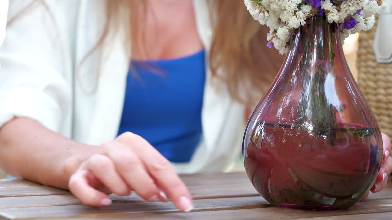 Close up of a woman's hands gesturing at a table with flowers on it at an outdoor cafe