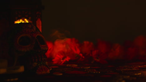 candles being blown out next to decorated skull with flowers celebrating mexican holiday of dia de muertos or day of the dead against dark background