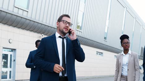 caucasian businessman in stylish clothes and glasses talking on the smartphone in the street