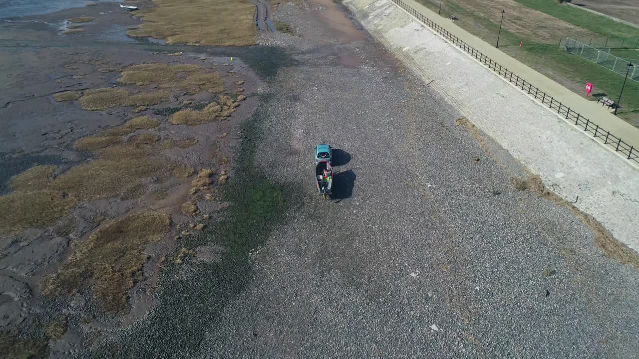 Drone flight tracking a car, towing a boat along the front at Lytham. The drone provides an aerial view of the coastline and stony beach