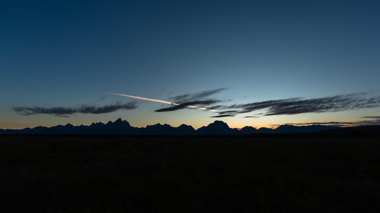 Mountain silhouettes at dusk with a colorful sky and contrail