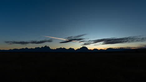 mountain silhouettes at dusk with a colorful sky and contrail