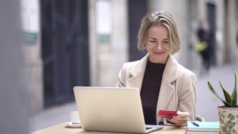 mujer de mediana edad con tarjeta de crédito y usando una computadora portátil para hacer compras en línea o banca por internet, gastando dinero electrónico para comprar regalos