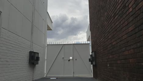 gated security door with spikes between two high walls, cloud time lapse in the background rolling by