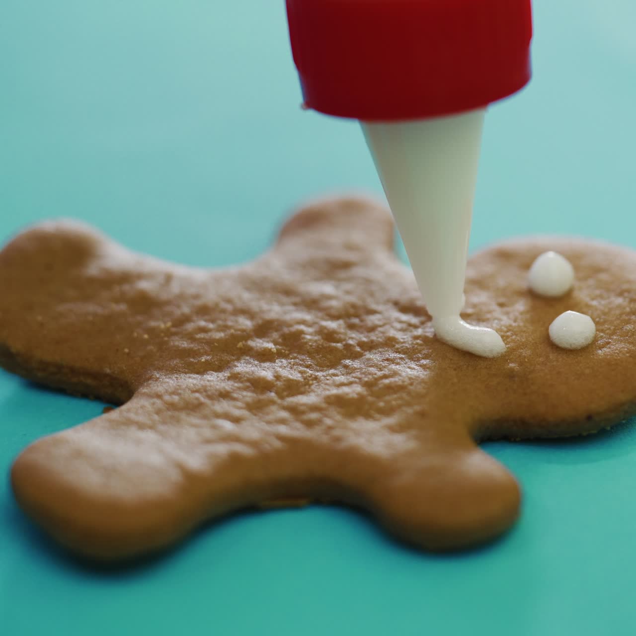 confectioner is painting cookies in the form of a ginger man on the New Year on the table in the kitchen. The process of decorating by glaze. Close-up