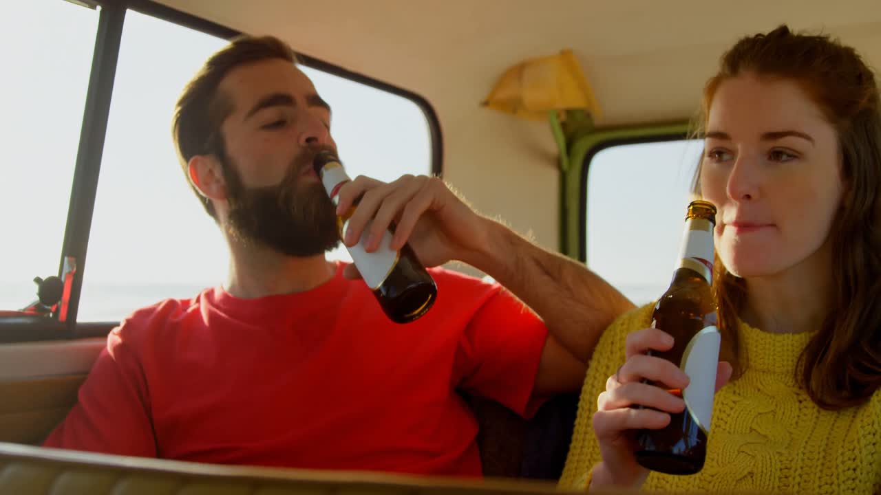 una pareja joven bebiendo cerveza en una furgoneta 4k.