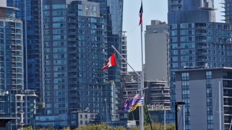 Canadian-flag-flying-in-the-city-park-during-the-daytime-with-the-skyscrapers-in-the-background,-Vancouver,-British-Columbia,-Canada