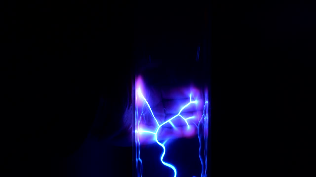 Closeup of the hand that is touching plasma lamp with neon electric beams on the black background