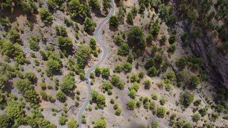 Camión-De-Pasajeros-A-Lo-Largo-De-Un-Camino-Sinuoso-En-Un-Paisaje-árido-Con-árboles-Y-Arbustos-Verdes,-Heirro,-España---Vista-Aérea-Desde-Un-Dron