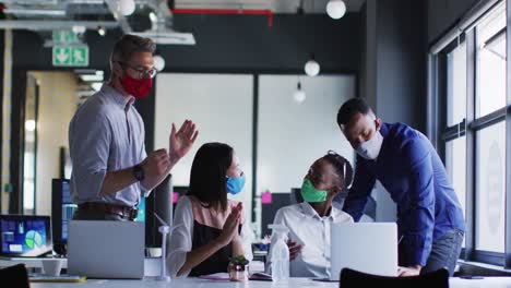 office colleagues wearing face masks clapping together at modern office