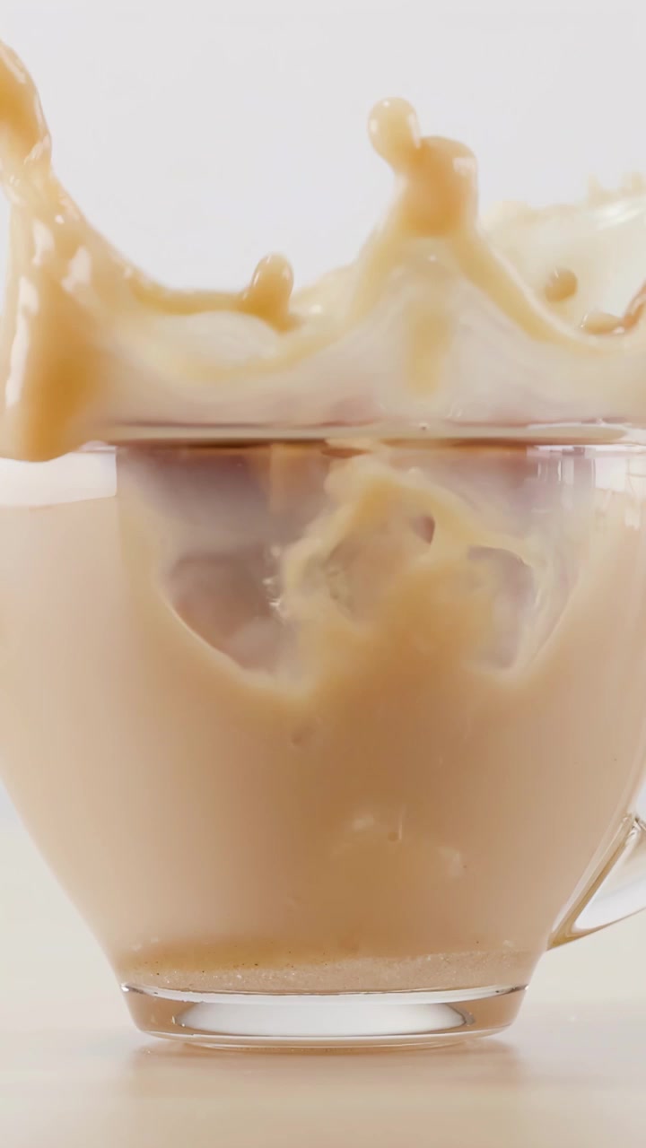 Zolletta di zucchero che cade in una tazza di vetro di caffè con latte
