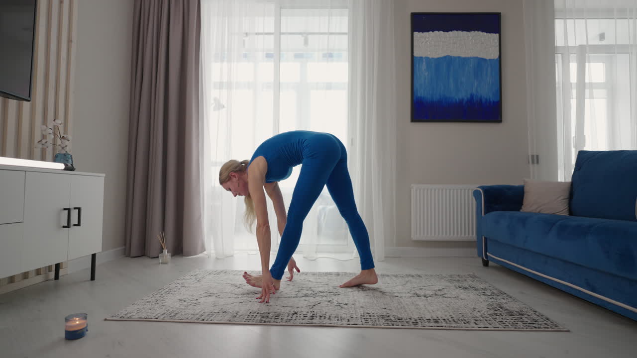 una mujer joven está practicando yoga en casa relajándose en una posición corporal simple sentada en el suelo con hermosos muebles a su alrededor. una mujer delgada con ropa deportiva de pie de rodillas inclinada hacia atrás y haciendo una postura de camello