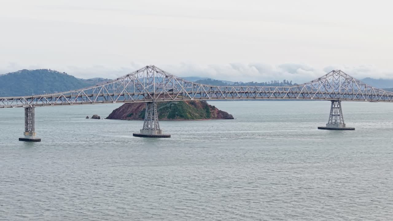 Aerial drone footage showcases the long expanse of the Richmond–San Rafael Bridge framed by tranquil water and a distant urban skyline.