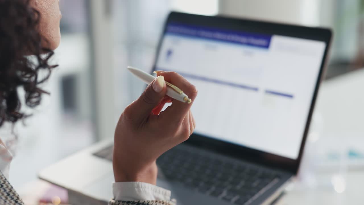 Woman working on laptop with pen in hand
