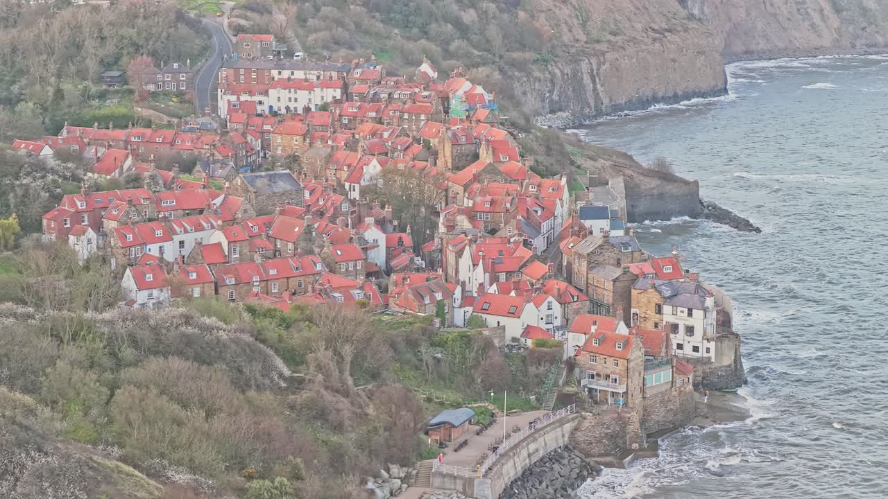 Baia di Robin Hood a Fylingdales vicino a Whitby, North Yorkshire, all'interno del Parco Nazionale North York Moors, che mostra un denso villaggio sulla scogliera, strade acciottolate e una costa rocciosa lungo la costa fossile giurassica.