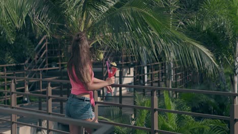 thin-girl-stands-on-bridge-leans-on-brown-wooden-railings