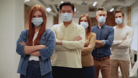 squadra di lavoro multietnica con maschera facciale guardando la telecamera in piedi. incontro di giovani uomini e donne d'affari.