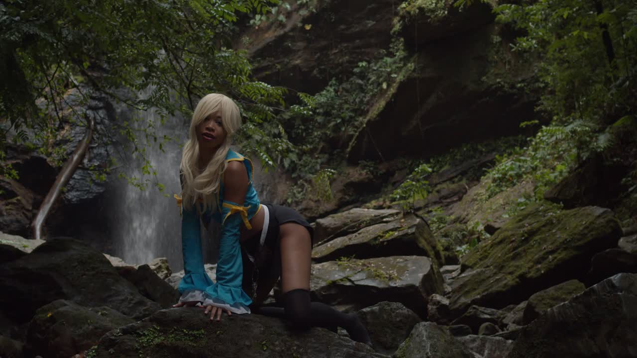 cosplayer de anime arrodillado sobre una gran roca en la base de una cascada ubicada en la isla caribeña de trinidad