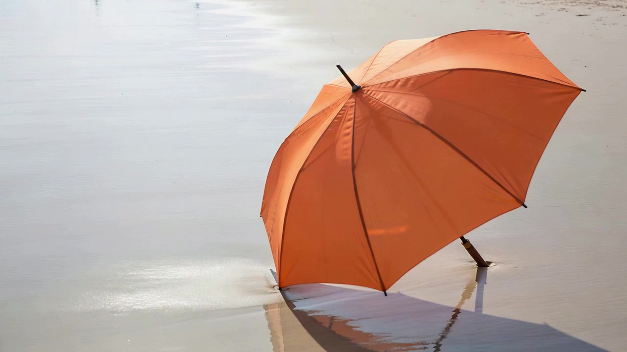 Skråtstillet orange parasol står på våd sandstrand, blide krusninger ændrer refleksionen, med plads til tekst.
