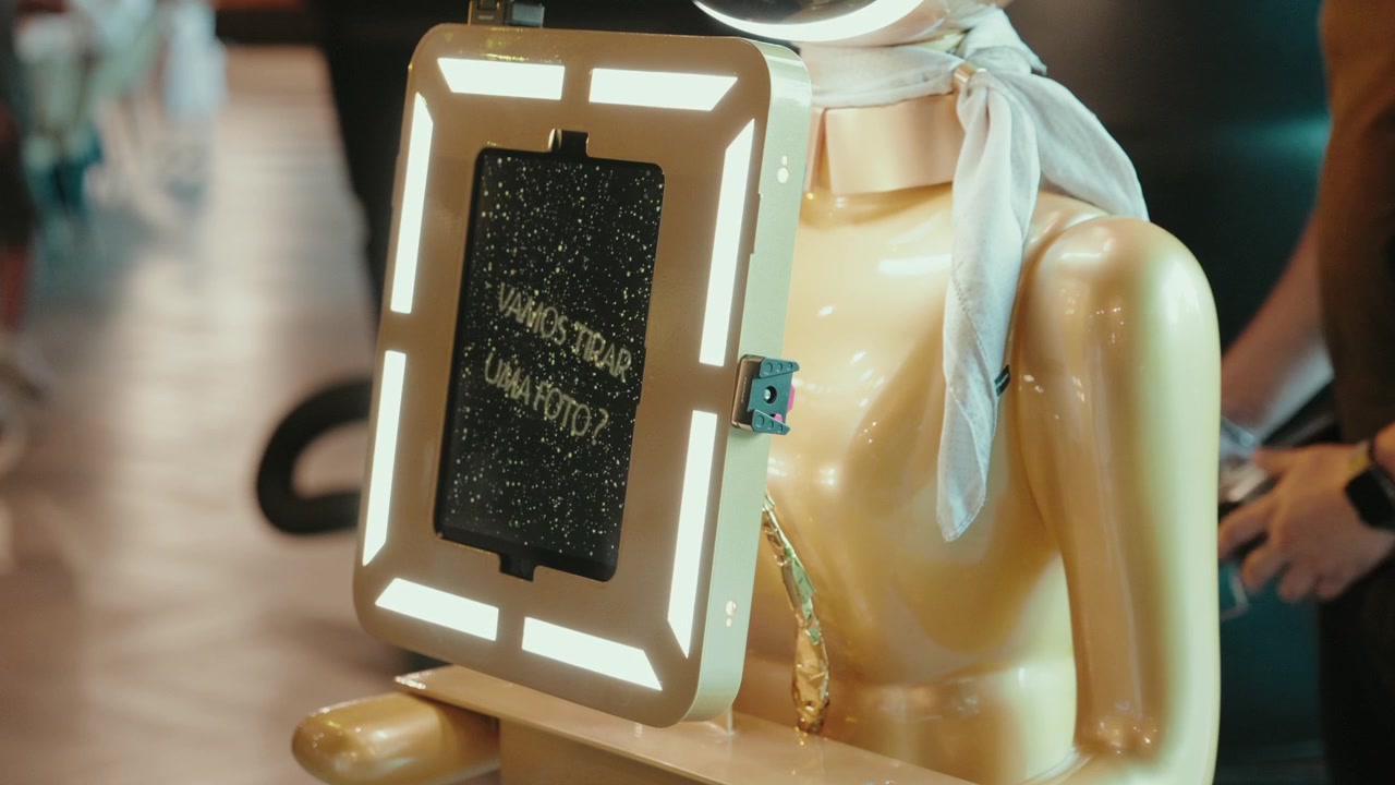 Cabina fotografica robot dorata con schermo tablet con ring light e messaggio in portoghese a un evento