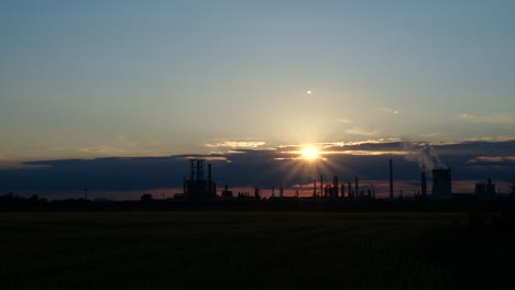 hazy sun setting down over wheat field with oil refinery silhouette on horizon, time lapse 4k