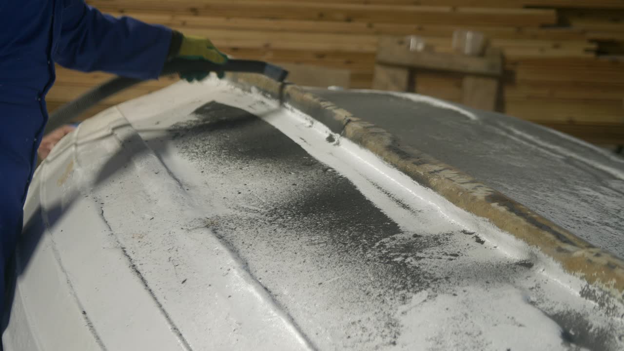 Vacuuming sanded depris from upturned boat hull in workshop