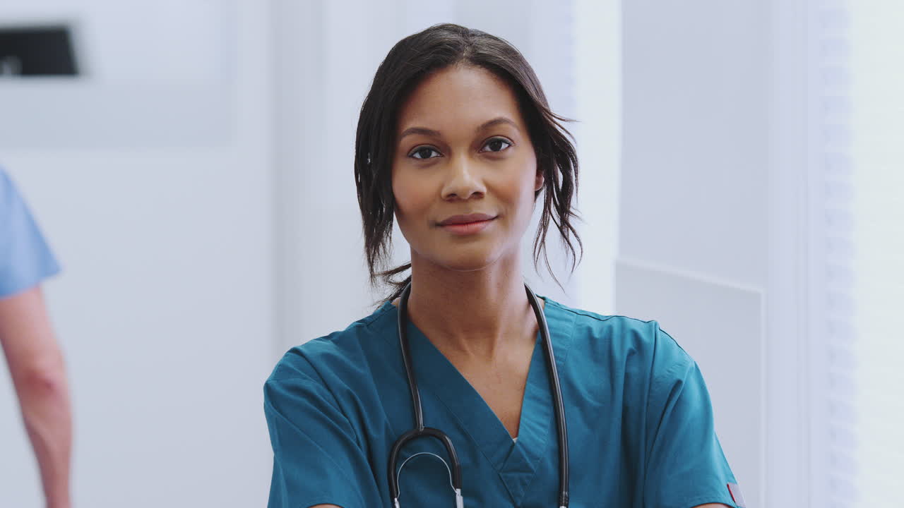 Portrait Of Female Doctor With Stethoscope Wearing Scrubs In Busy Hospital Corridor