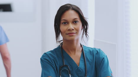 portrait of female doctor with stethoscope wearing scrubs in busy hospital corridor