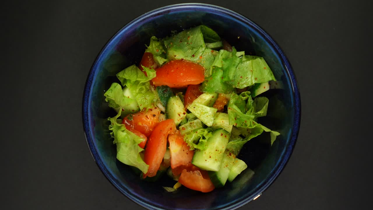 Bowl of salad is fast rotating on black background. Looping footage