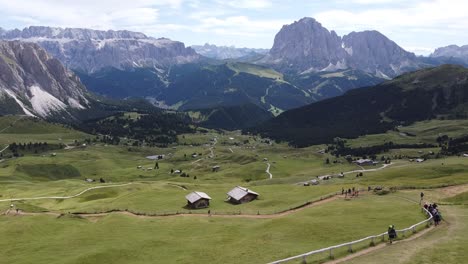 val gardena valley to the seceda mountain peak at south tyrol, italian alps, dolomites, italy - aerial drone view of hikers, green valley, cabins and mountains