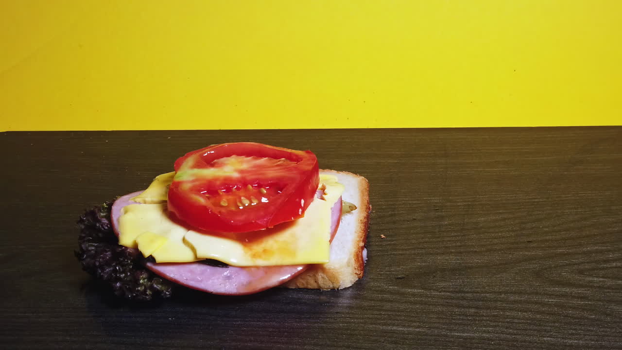Close-up shot of a sandwich falling in layers in front of a yellow background