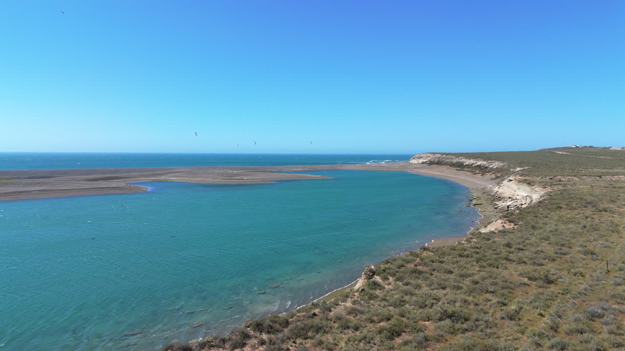 Aerial of rugged cliffs and shoreline at Punta Delgada, highlighting Península Valdés’ natural beauty coastline with birds flying above in open sky