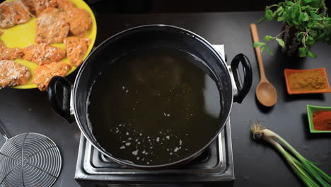 deep frying crispy chicken in oil in a black frying pan