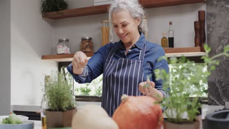 smiling senior caucasian woman seasoning vegetables in kitchen, slow motion