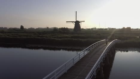 A-drone-shot-panning-right,-around-a-model-walking-on-a-bridge-and-looking-at-Dutch-Windmills-in-the-Netherlands-during-sunrise