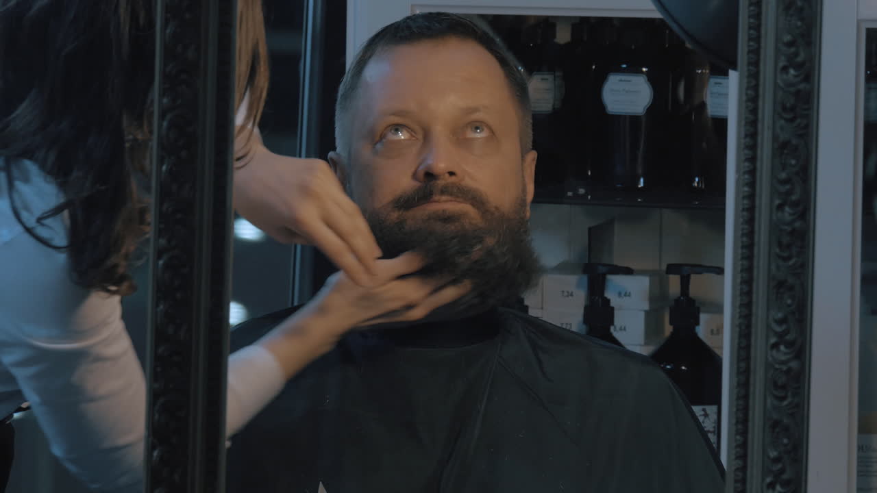 vista de cerca de la barbero mujer cuidando de la barba exuberante del barbero hombre aplicando cosméticos