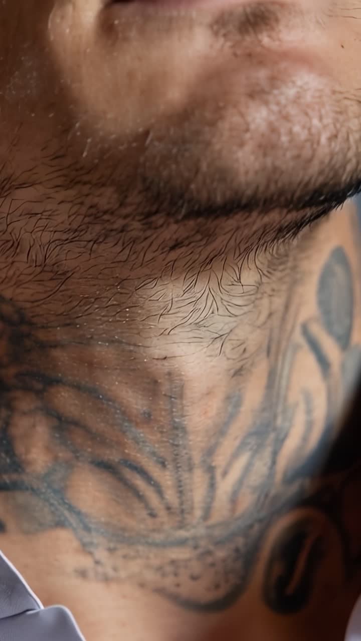 Close-up of man's lips and ear. Tattooed neck visible beneath white shirt collar. Silver hoop earring gleams softly. Man appears calm, relaxed, confident. Ideal for fashion, beauty