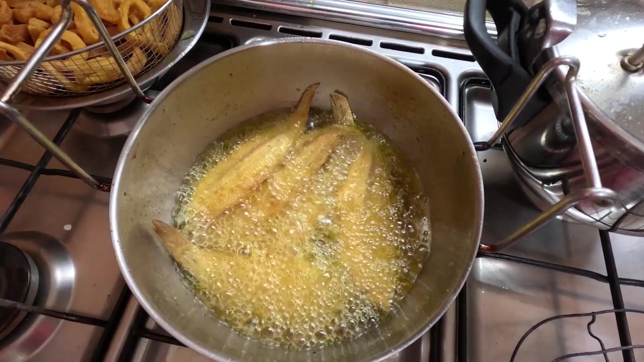 Crispy Moroccan sole fish pieces deep-fried in bubbling oil, lifted with a slotted spoon, showing traditional seafood street food preparation in a close-up cooking scene.