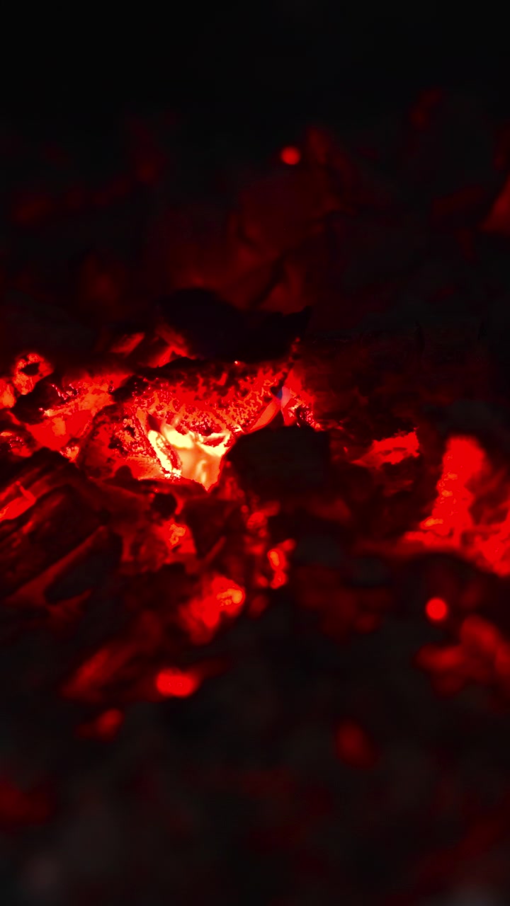 Glühende Holzkohleglut in der Dunkelheit, rote Kohlen glimmen mit schwebender Asche und feinen Funken, intensive Hitze.