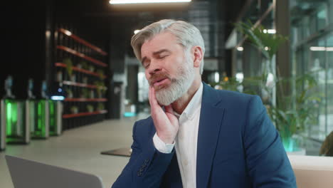 caucasian businessman in office lobby working on laptop and feeling toothache in modern office lobby