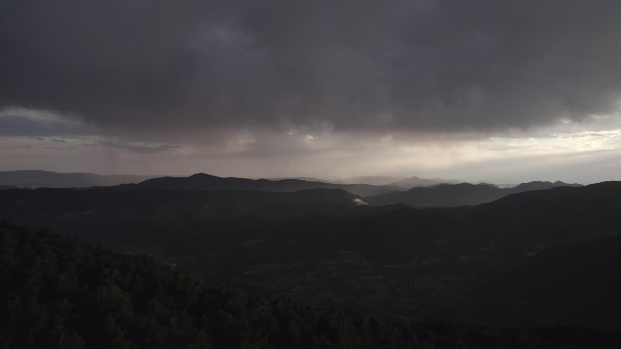 This drone video captures a stunning frontal descriptive shot over the Hecho Valley in the Aragonese Pyrenees, Spain, at sunset with dramatic cloudy skies and distant storms enhancing the scenery.