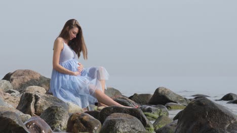 una mujer embarazada se sienta en las rocas, pensativa mientras sostiene su barriga y piensa en el futuro de sus bebés