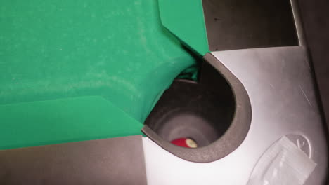 close-up upshot of red billiard ball rolling smoothly into pool table pocket on green surface. motion blur highlights movement, precision, and tension of shot, capturing accuracy