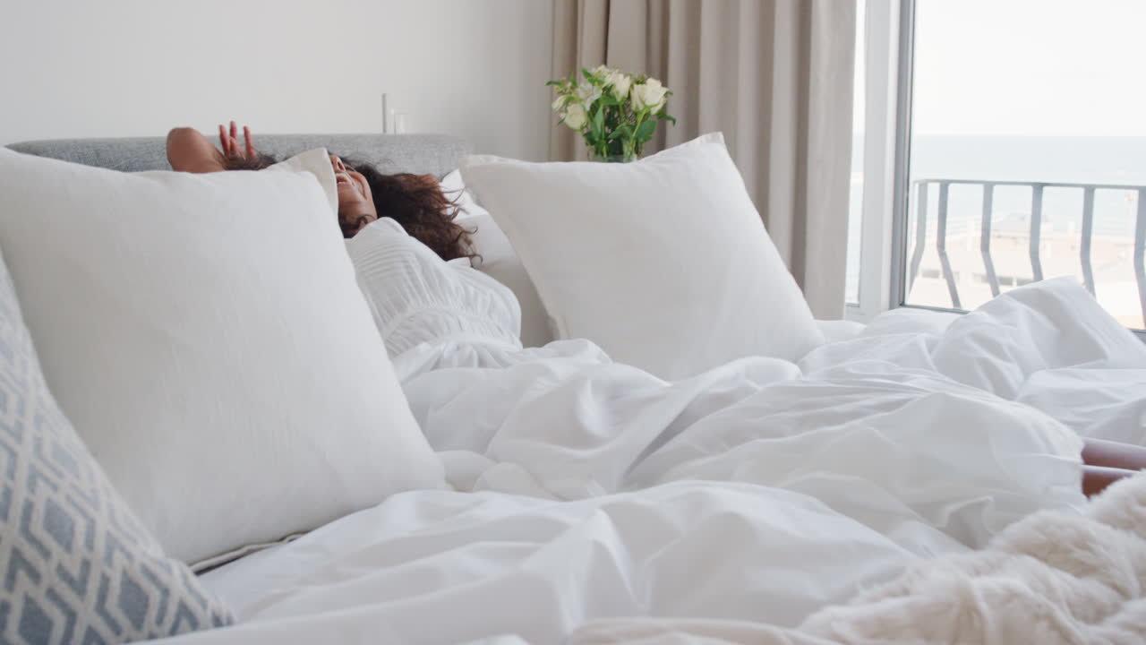 행복한 여성이 침대에 뛰어들고 재미있게 웃고 독립적인 생활 방식을 즐기며 자유를 축하합니다.