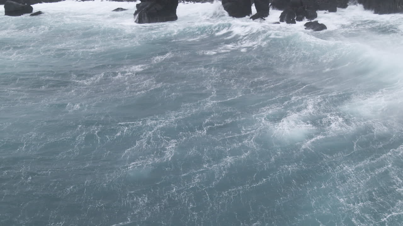 아이슬란드 해변의 공중 촬영 바위와 구름이 많은 날 지평선을 지켜보는 사람들의 파도를 통해