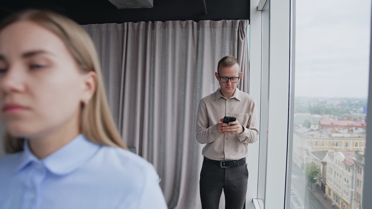 Young man looking at phone in his hands. Male colleague comes up to a female feeling bad and having headache. Coworker tries to comfort and aid lady.