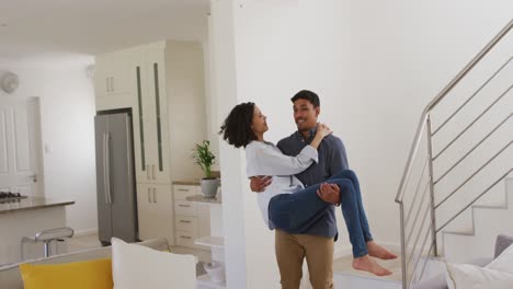 Happy-romantic-hispanic-man-carrying-woman-downstairs-in-living-room